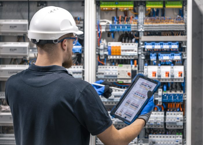 Electrical technician working in a switchboard with fuses, uses a tablet. Electrical technician looking focused while working in a switchboard with fuses. SSUCv3H4sIAAAAAAAACpySwW7CMAyG75P2DlXOVKItpcCroB2cxNCIkFRJyjQh3n1O0qLsukOl+rP923/d5+dHVTEOXgl2qp4xolhpPfvgIChrCG83C3doJLqSPFy335YAVBmhVME6BbqEHIIYDdyRoJm1jviVkswHCLNHH3dZkICAV9LI8C2RFz7nuFoTKUkdlGJsUzA/88RWlMX/1Zlfvt6Gr2jET1q4MOJQI2Qj51zKbt8B3b20BrNUtnD1sAJ0LOgKJVATOPjTNzkllLkWxIYx3WVVEnY2wcWt3maYtnYCruNXv9AYXPkI3lO5XHkxW9BfYO/FHGND8rSoMknHiWHTdf2+HTp6hsN+aLftUpAPOirSSeusQhSLm5KlKxU3YAcx4JEfd/UFGqx3fQ81b2Rfiwv0TXNoObQd3eL1CwAA//8DABhKQXa5AgAA